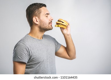 Young Man Holding A Piece Of Hamburger. Student Eats Fast Food. Burger Is Not Helpful Food. Very Hungry Guy. Diet Concept.