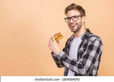 Young man holding a piece of hamburger. Student eats fast food. Burger is not helpful food. Very hungry guy. Diet concept. Isolated over beige background.