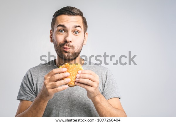 ハンバーガーを持つ若い男性 学生はファストフードを食べる ハンバーガーは役に立たない食べ物だ お腹が空いた男 国会のコンセプト の写真素材 今すぐ編集