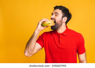 Young man holding a piece of sandwich. Student eats fast food. Burger is not helpful food. Very hungry guy. Diet concept. Isolated over yellow background.
