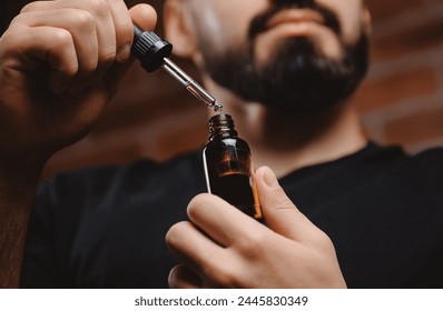 Young man holding pipette with oil for beard hair. Concept spa cosmetic and treatment wellness and natural beauty of skin men. - Powered by Shutterstock