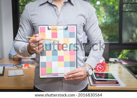 Young man holding and point to a color chart for home design. Graphic designers working on color chart at modern office.