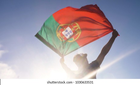 Young man holding portuguese national flag to the sky with two hands at the beach at sunset portugal