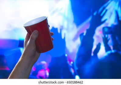 Young Man Holding Red Party Cup In Nightclub Dance Floor. Alcohol Container In Hand In Disco. College Student Having Fun And Dancing. Celebrating People In The Back. Event Marketing And Promotion.