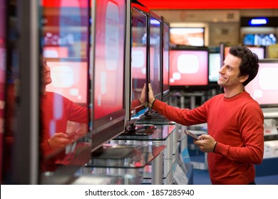 Young Man Holding A Remote Control In Hand And Standing In The Middle Of An Electronics Appliances Store While Shopping Or A New Television