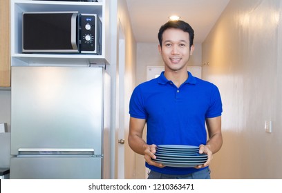 Young Man Holding Stack Of Plates In The Modern Kitchen