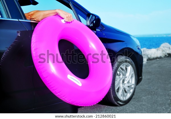 young man holding a swim ring outside of the window\
of a car
