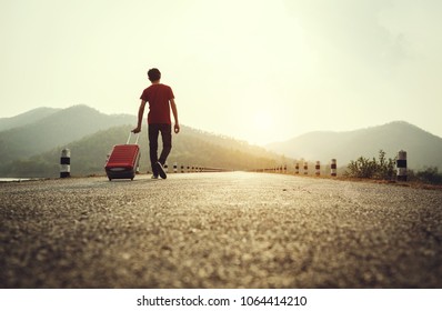 Young Man Holding Travel Bag Walking On The Roadway, Summer Nature Outdoor.