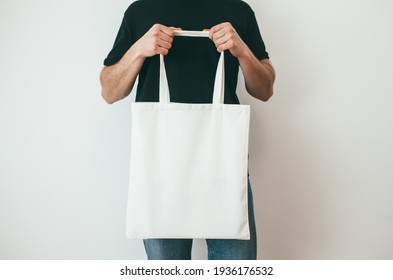 Young Man Is Holding White Textile Eco Bag On White Background. Mockup For Design