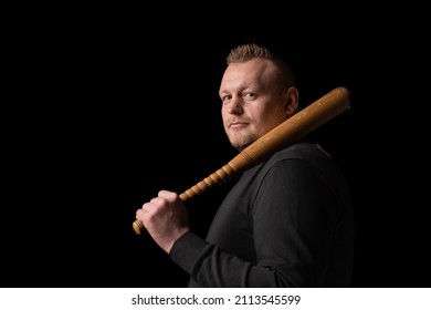 A Young Man Is Holding A Wooden Bat. Bouncer, Security Guard, Bodyguard Concept. A Large Man In A T-shirt Looks At The Camera.