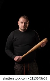 A Young Man Is Holding A Wooden Bat. Bouncer, Security Guard, Bodyguard Concept. A Large Man In A T-shirt Looks At The Camera.