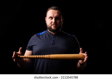 A Young Man Is Holding A Wooden Bat. Bouncer, Security Guard, Bodyguard Concept. A Large Man In A T-shirt Looks At The Camera.