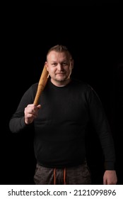 A Young Man Is Holding A Wooden Bat. Bouncer, Security Guard, Bodyguard Concept. A Large Man In A T-shirt Looks At The Camera.