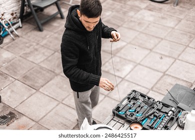 A young man holds a brake wire for a bike while standing in the backyard of a house. - Powered by Shutterstock