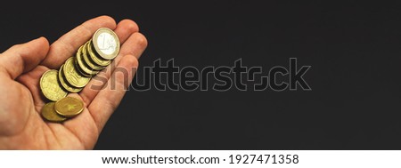 Young man holds euro coins, banner or panorama photo on black background, copy space image