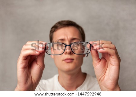 the young man holds glasses with diopter lenses and looks through them, the problem of myopia, vision correction