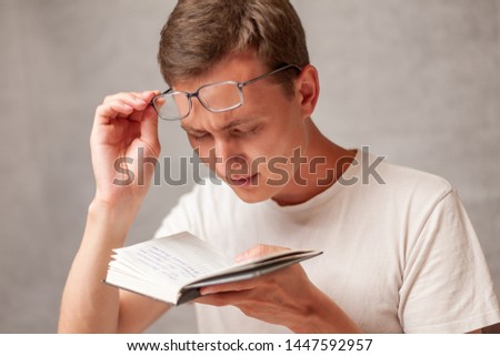 the young man holds glasses with diopter lenses and looking at the book, the problem of myopia, vision correction