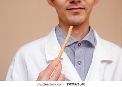 A young man holds a miswak (siwak) in a white coat. arak tree, Salvadora persica, sunnah. Beige background