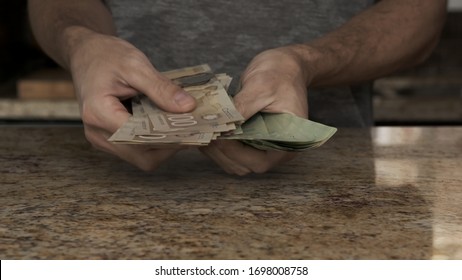 A Young Man Holds Money In His Hands. A Guy Counts The Canadian Dollars That He Took Out Of The Envelope. A Young Husband Recounts A Large Amount Of Money. Counting Money In A Kitchen Payday