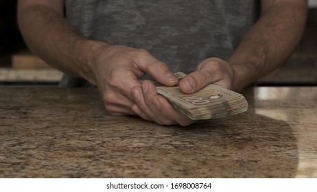 A Young Man Holds Money In His Hands. A Guy Counts The Canadian Dollars That He Took Out Of The Envelope. A Young Husband Recounts A Large Amount Of Money. Counting Money In A Kitchen Payday