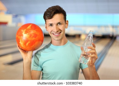 Young Man Holds Orange Ball And Bottle With Water In Bowling Club; Shallow Depth Of Field