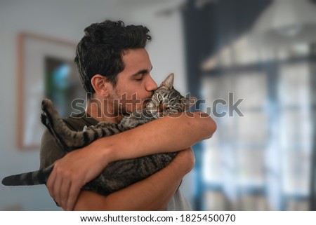 young man holds a tabby cat in his arms and kisses it