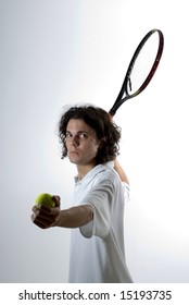 A Young Man, Holds A Tennis Racket Back And A Ball Forward, Getting Ready To Serve The Ball. He Stares At The Camera. Vertically Framed Shot.