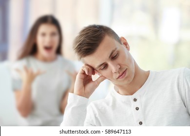 Young Man At Home With Blurred Angry Girlfriend On Background