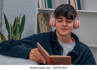 young man at home reading book and listening to music with headphones - Powered by Shutterstock