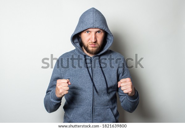 Young man in a hood with a serious,\
aggressive face and a fighting stance on a light\
background