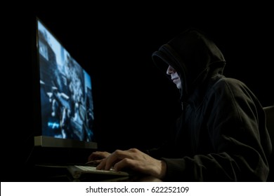 Young man with hoodie playing computer games in dark room