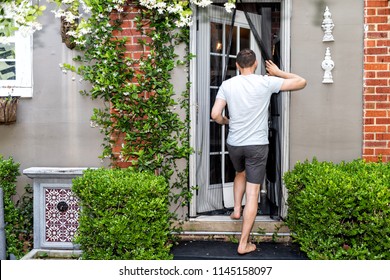 Young man, house, entering outdoor spring garden with hanging plant flowers covering brick wall in backyard porch of home by door, insect mosquito pest net
