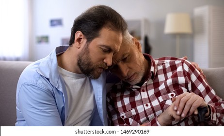 Young man hugging and comforting depressed old dad, suffering melancholy, loss