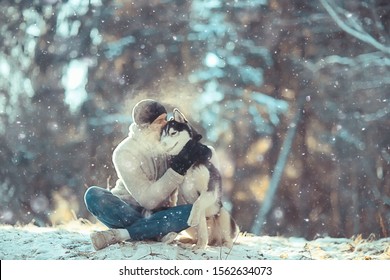 Young Man Hugs A Husky Dog In The Winter In The Forest, A Man And A Dog Hug Together And Play In A Winter Nature Landscape