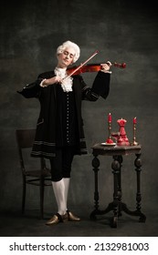 Young Man In Image Of Amadeus Mozart, Medieval Person Isolated On Dark Vintage Background. Retro Style, Comparison Of Eras Concept. Elegant Male Model As Historical Character, Great Music Compose