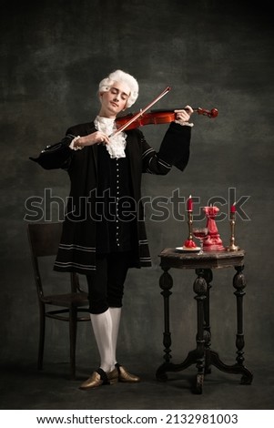 Young man in image of Amadeus Mozart, medieval person isolated on dark vintage background. Retro style, comparison of eras concept. Elegant male model as historical character, great music compose