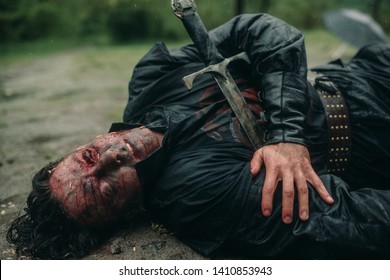 A Young Man In The Image Of A Murdered Medieval Knight Lying On The Ground And With Worms Crawling On His Face. Top View.