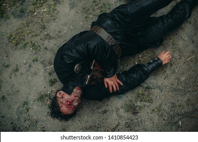 A Young Man In The Image Of A Murdered Medieval Knight Lying On The Ground And With Worms Crawling On His Face. Top View.