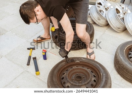 A young man independently disassembles a car tire using a crowbar.