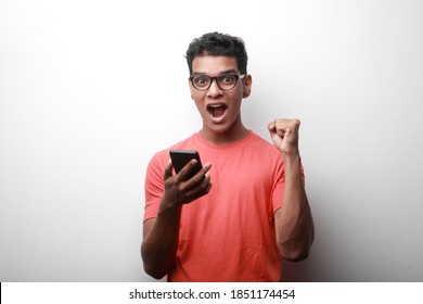 Young man of Indian origin holding his mobile phone with an excited face