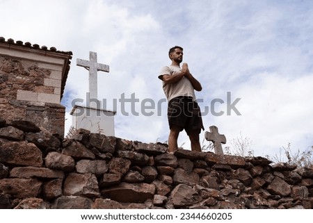 The young man of Indian origin takes a breath and prays next to a cross in a stone church cemetery.