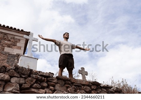 The young man of Indian origin takes a breath and stretches out his arms next to a cross in a stone church cemetery.