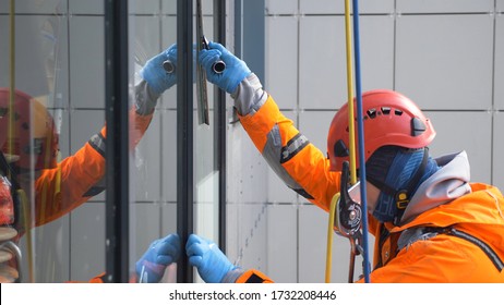 Young Man Industrial Climber In Bright Suit And Helmet Washes Windows At A Height Close Up