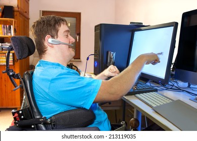 A young man with infantile cerebral palsy caused by a complicated birth sitting in a multifunctional wheelchair using a computer with a wireless headset reaching out to touch the touch screen - Powered by Shutterstock