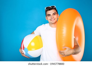 Young man with inflatable ball and ring on blue background - Shutterstock ID 1945778800