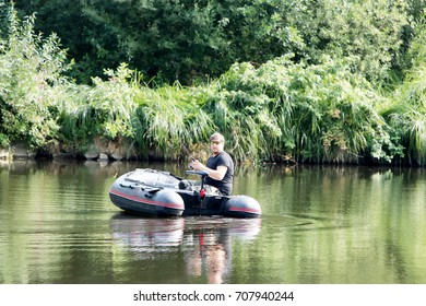 Young Man In Inflatable Boat With Electric Outboard Fishing At River.