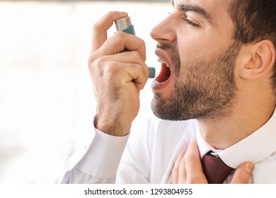 Young Man With Inhaler Having Asthma Attack In Office