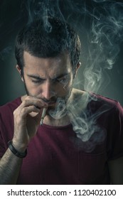 Young Man Inhaling A Rich Cloud Of Smoke, Studio Image, Black Background