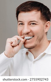 Young man inserts a clear aligner tray while smiling, demonstrating at-home orthodontic care, dental hygiene and confident oral health. Casual close-up portrait in a white shirt for lifestyle and self-care.