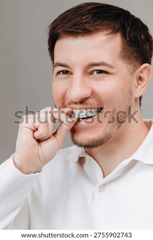 Young man inserts a clear aligner tray while smiling, demonstrating at-home orthodontic care, dental hygiene and confident oral health. Casual close-up portrait in a white shirt for lifestyle and self-care.
